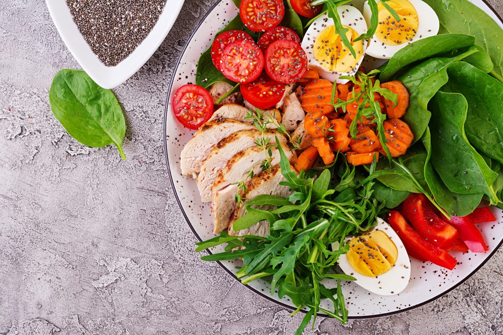 Plate with a keto diet food. Cherry tomatoes, chicken breast, eggs, carrot, salad with arugula and spinach. Keto lunch. Top view